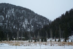 Paisagem montanhosa com uma cabana rodeada por árvores cobertas de neve e um céu limpo.