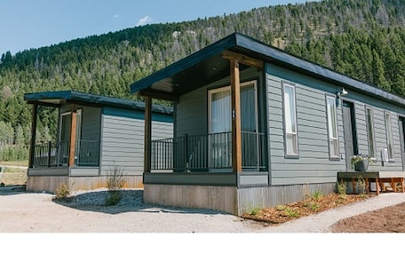 Two cabins with a covered porch, set against a forested hillside.