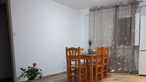 Un comedor con una mesa y sillas de madera, una planta en maceta y una ventana con cortinas translúcidas.