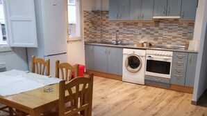 Una cocina moderna con armarios grises, lavadora integrada y un comedor con sillas y mesa de madera.