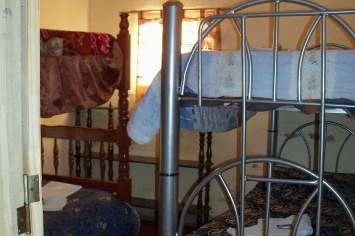 Una habitación con dos literas, una de madera y otra de metal, una silla de madera y una mesita pequeña.