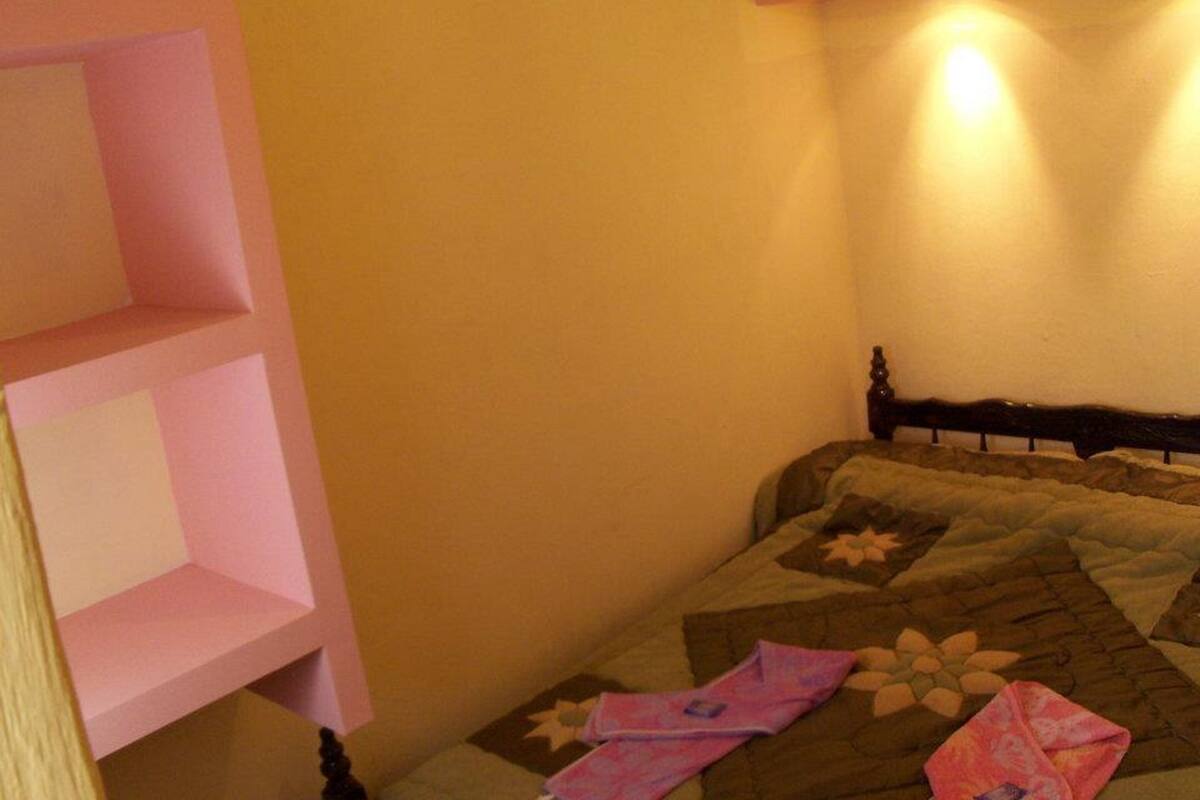 Un dormitorio con una cama, una estantería rosa y una lámpara de pared.
