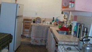 Een kleine keuken met een koelkast, fornuis, gootsteen en diverse keukenbenodigdheden op het aanrecht.