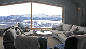 A living room with a large window, a grey sofa, a round coffee table, and two armchairs. - Hemavans Högfjällshotell (Hemavan)