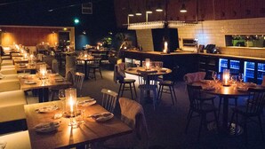 A dimly lit restaurant with tables set for dining, featuring candles and a bar area with a digital display. - Hemavans Högfjällshotell (Hemavan)