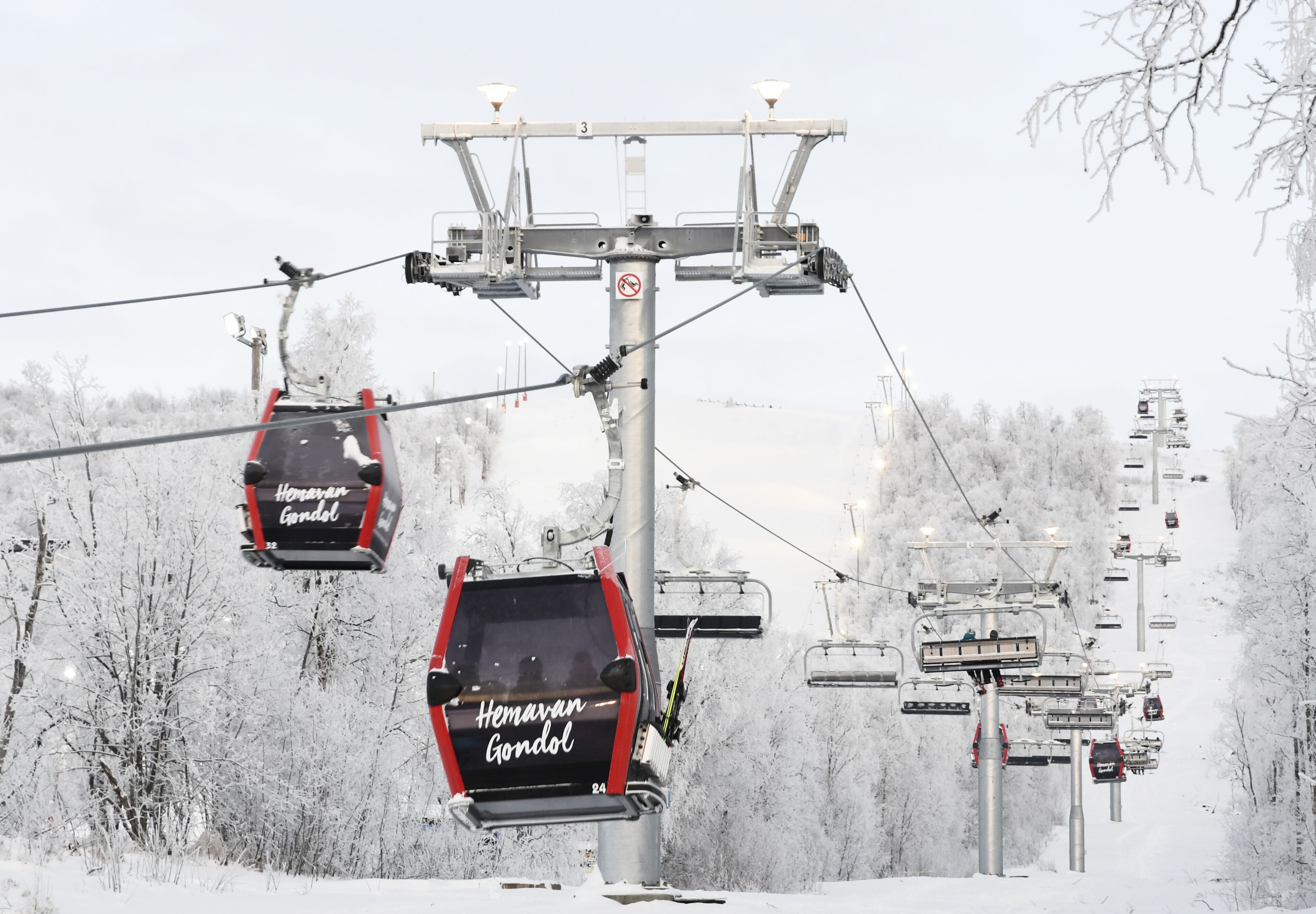 A ski lift with cabins labeled "Hemavan Gondol" in a snowy landscape.