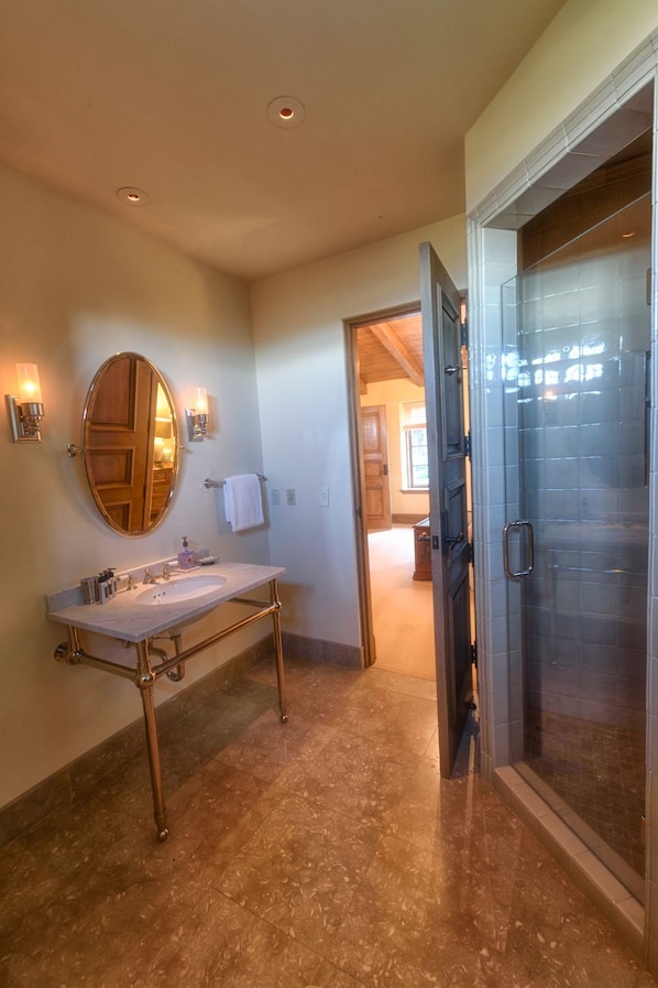 Un baño con tocador, espejo redondo y cabina de ducha de vidrio.