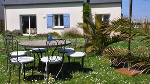 A house with a patio area featuring a round table and four chairs, surrounded by a garden with various plants and flowers. - Large, bright house with south-facing garden near the beach.  (Brignogan-Plage)