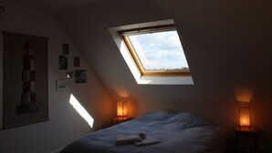 A bedroom with a skylight, a bed with a striped bedspread, two bedside tables with lamps, and a poster on the wall. - Large, bright house with south-facing garden near the beach.  (Brignogan-Plage)