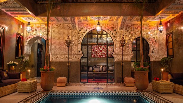 A luxurious indoor pool area with ornate arches, a seating area with sofas, and decorative lighting. - Riad Touda (Marrakech)