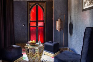 Una habitación con una puerta de marco rojo, una mesa con diseño y dos sillones tapizados en azul oscuro.