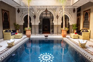 Un área de piscina con elaborados detalles en mosaicos, asientos con cojines y plantas en macetas.