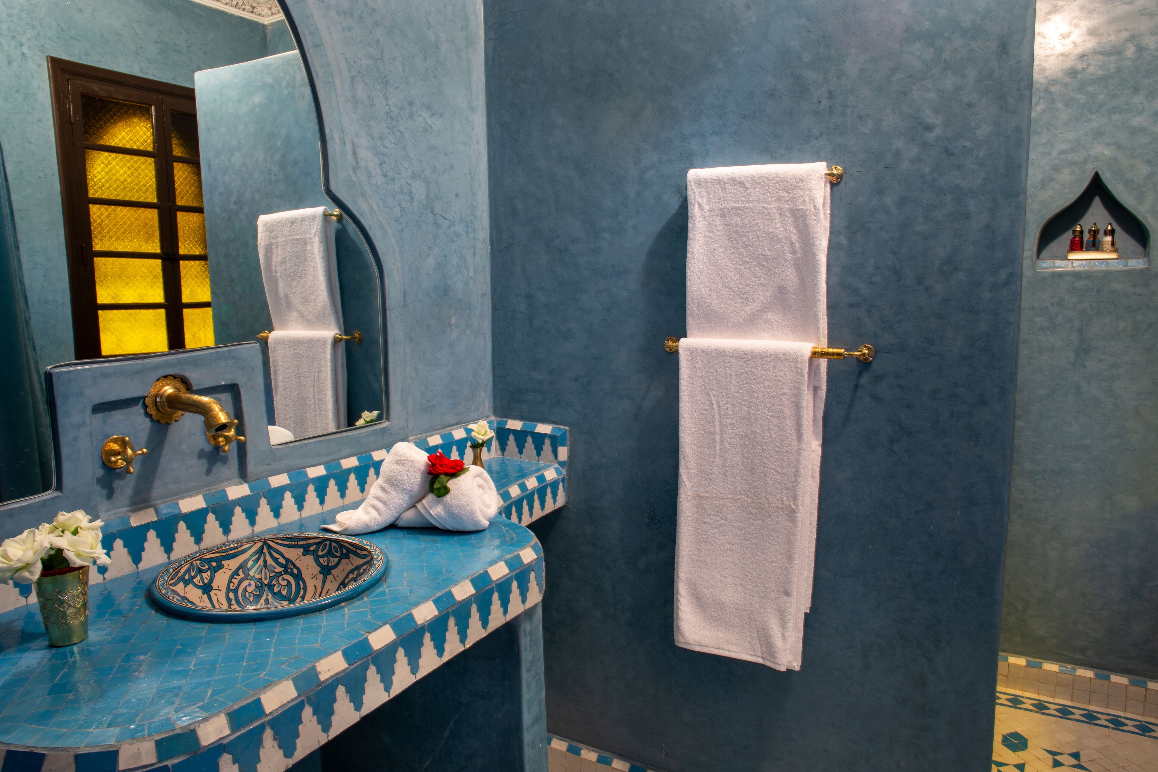 A bathroom with a blue and white tiled sink, a gold faucet, a white towel hanging on a towel rack, and a small decorative shelf with figurines.