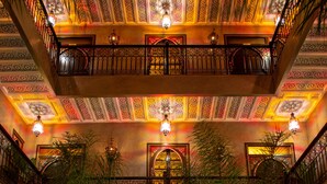 A luxurious indoor pool area with ornate ceiling designs, a central fireplace, and potted plants. - Riad Touda (Marrakech)