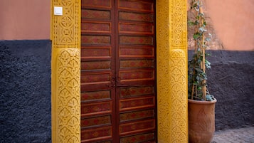 A traditional yellow door with intricate patterns, a potted plant beside it, and a tiled entrance.
