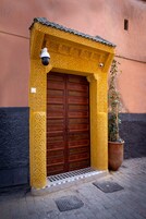 Una puerta amarilla tradicional con diseños intrincados, una planta en maceta a un lado y un acceso con baldosas.