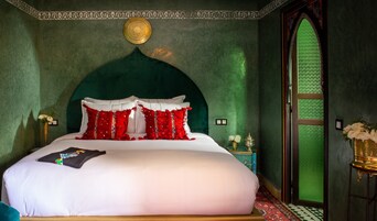 Un dormitorio con una cama grande, paredes verdes, un techo decorativo y una puerta verde.