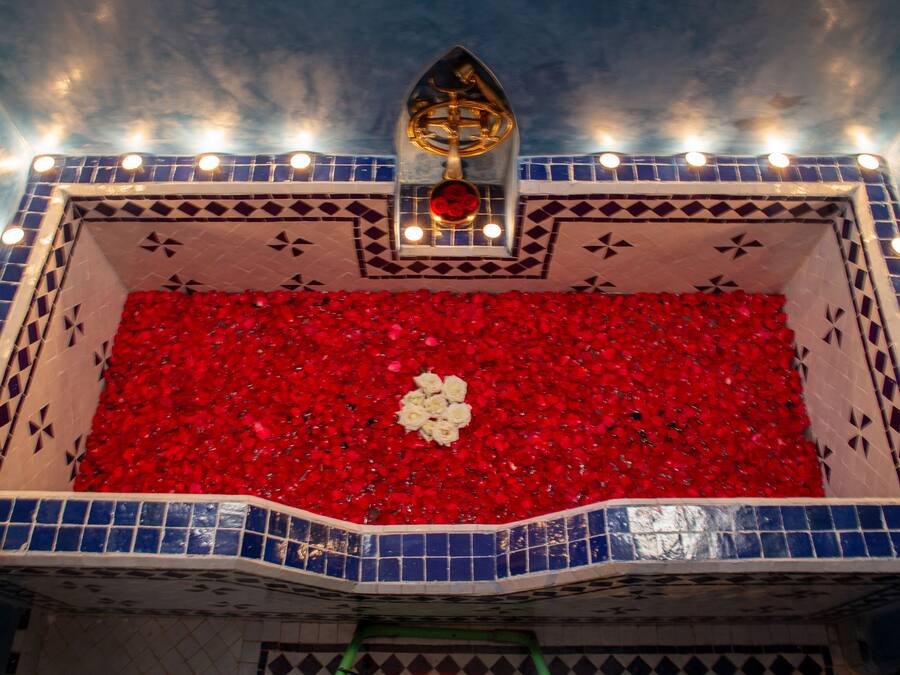 Una bañera con pétalos de rosa roja y un objeto dorado en el techo.