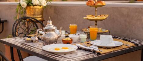 A breakfast setup with a tiered stand holding pastries, a teapot, and a jug of orange juice on a table with a woven placemat.