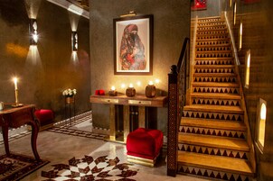 Una escalera con un diseño ornamental, un banco de terciopelo rojo, un cuadro colgado en la pared y una mesa con velas.
