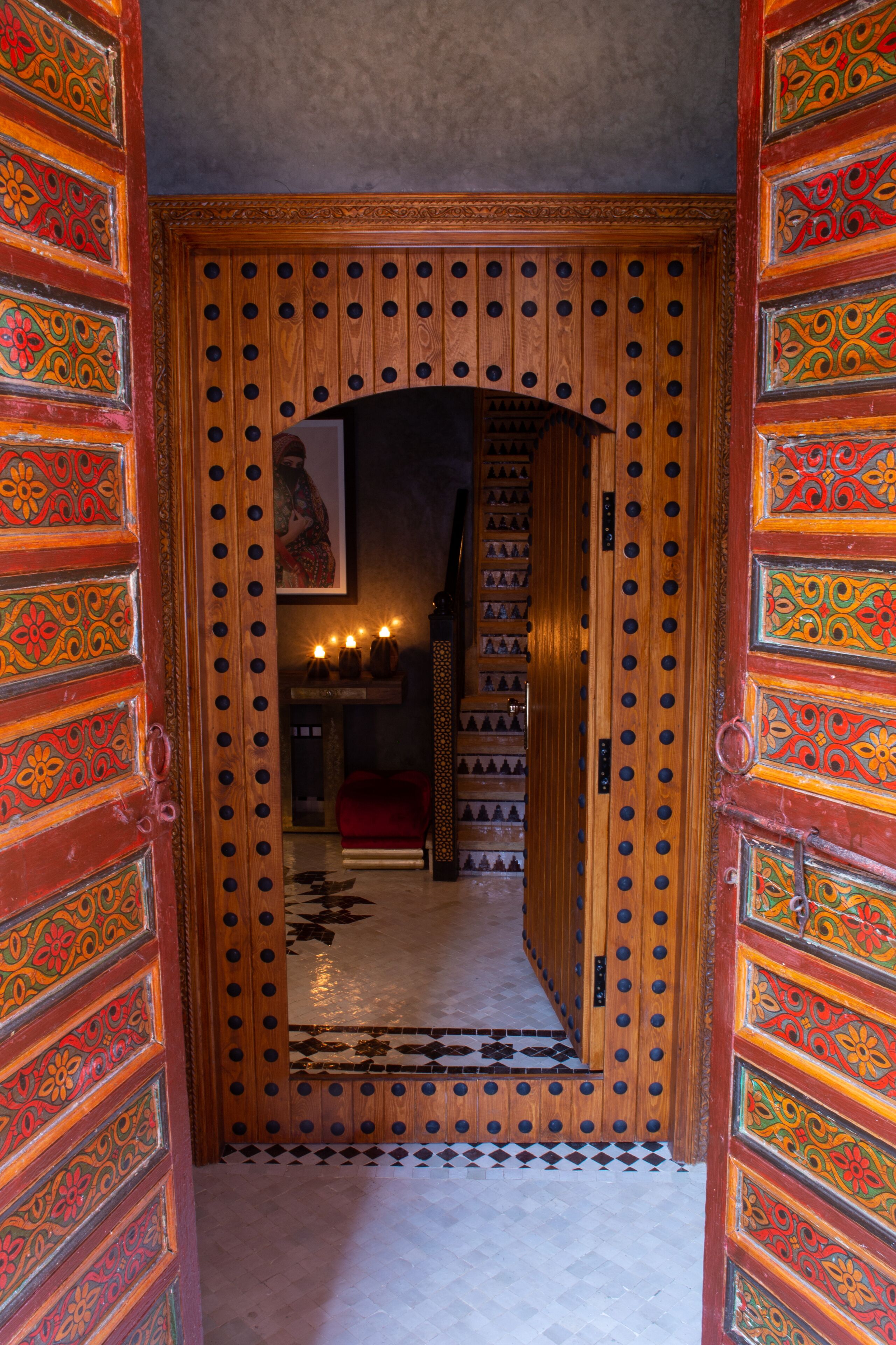 An ornate wooden door with intricate patterns and a mirror reflecting a staircase.