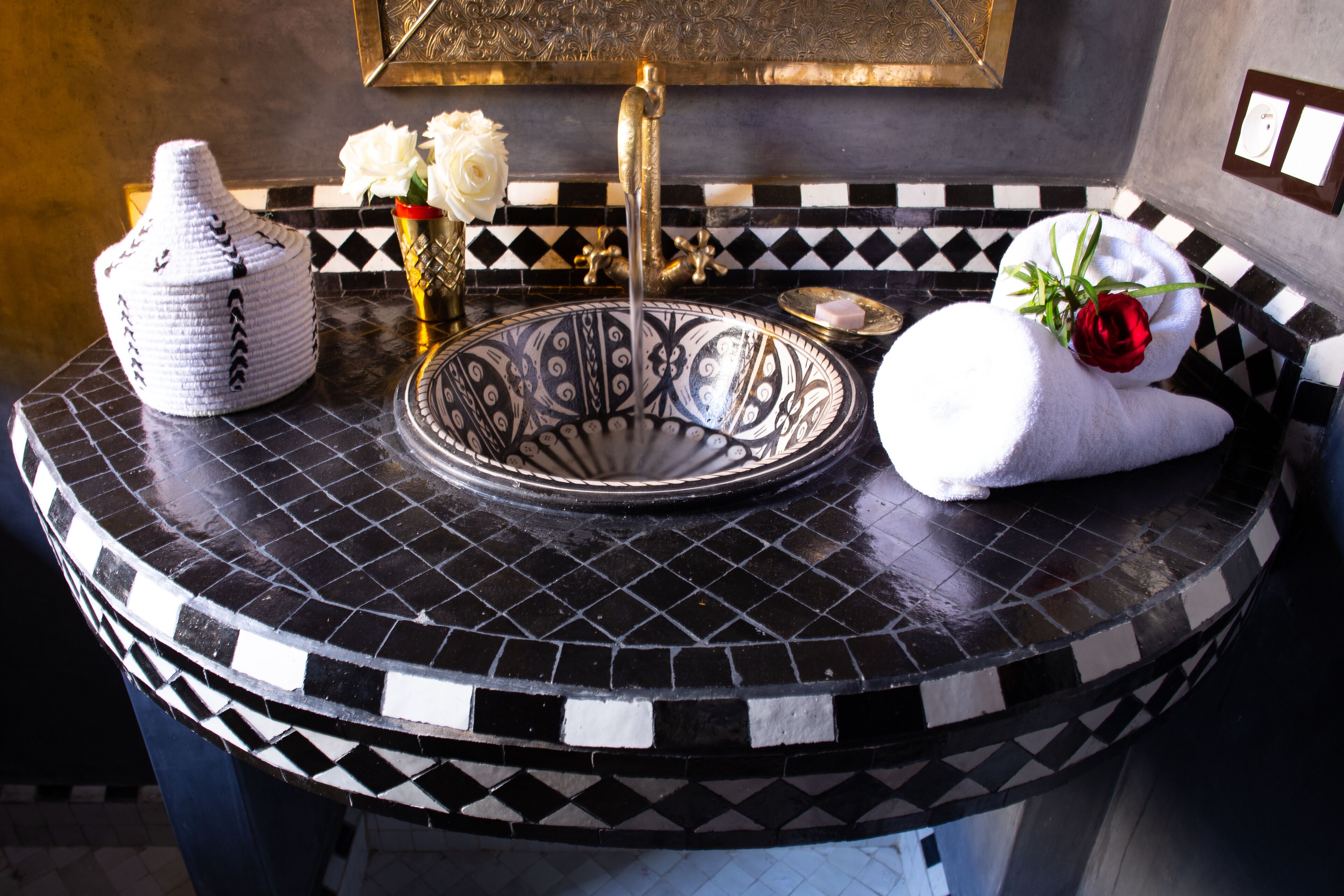 A bathroom with a black and white checkered tile backsplash, a white vase with a red rose, and a white towel with a red rose.