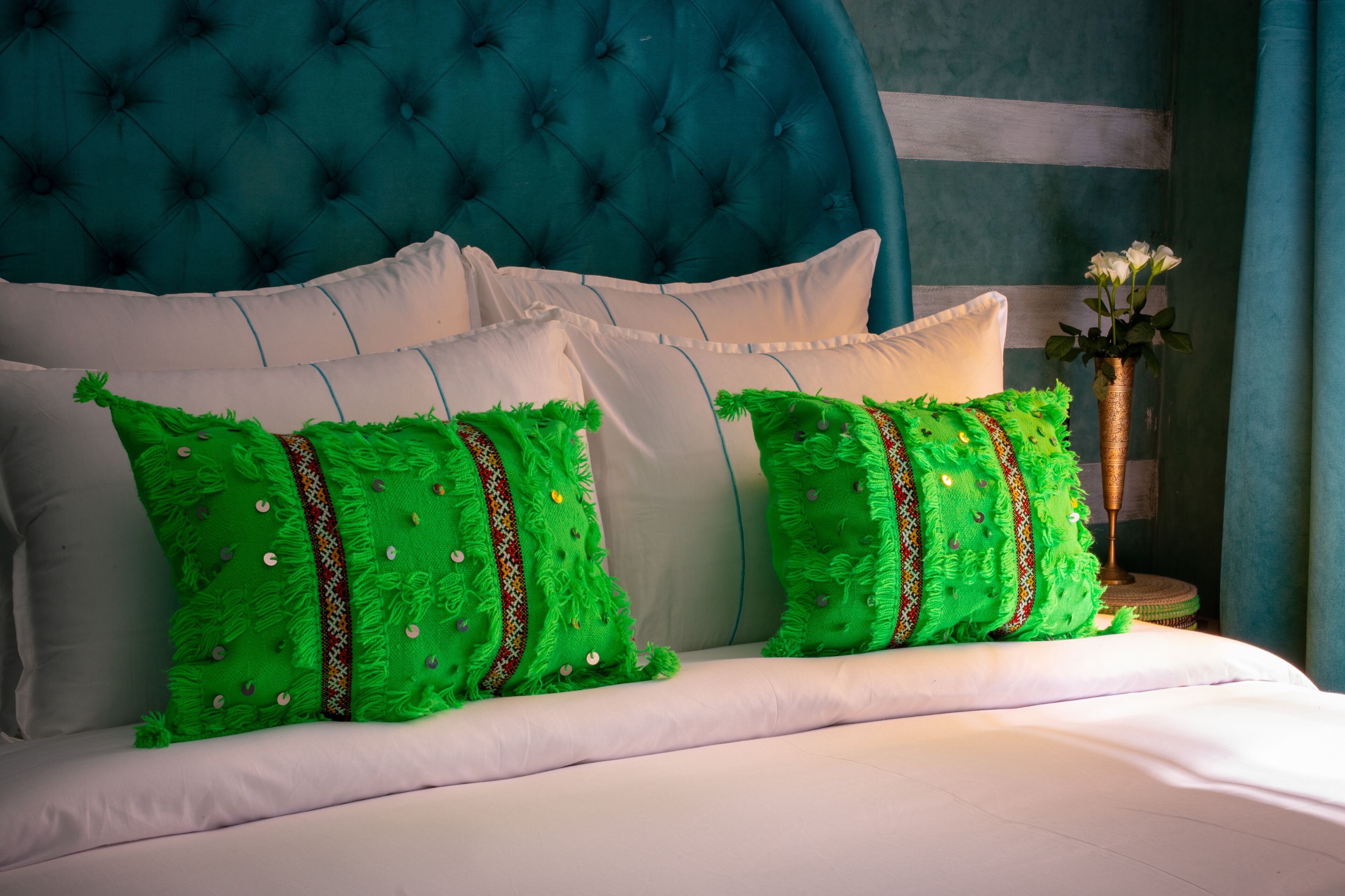 Cama com lençóis brancos e almofadas verdes com padrões decorativos.