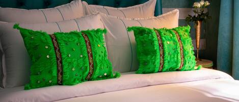 Cama com lençóis brancos e almofadas verdes com padrões decorativos.