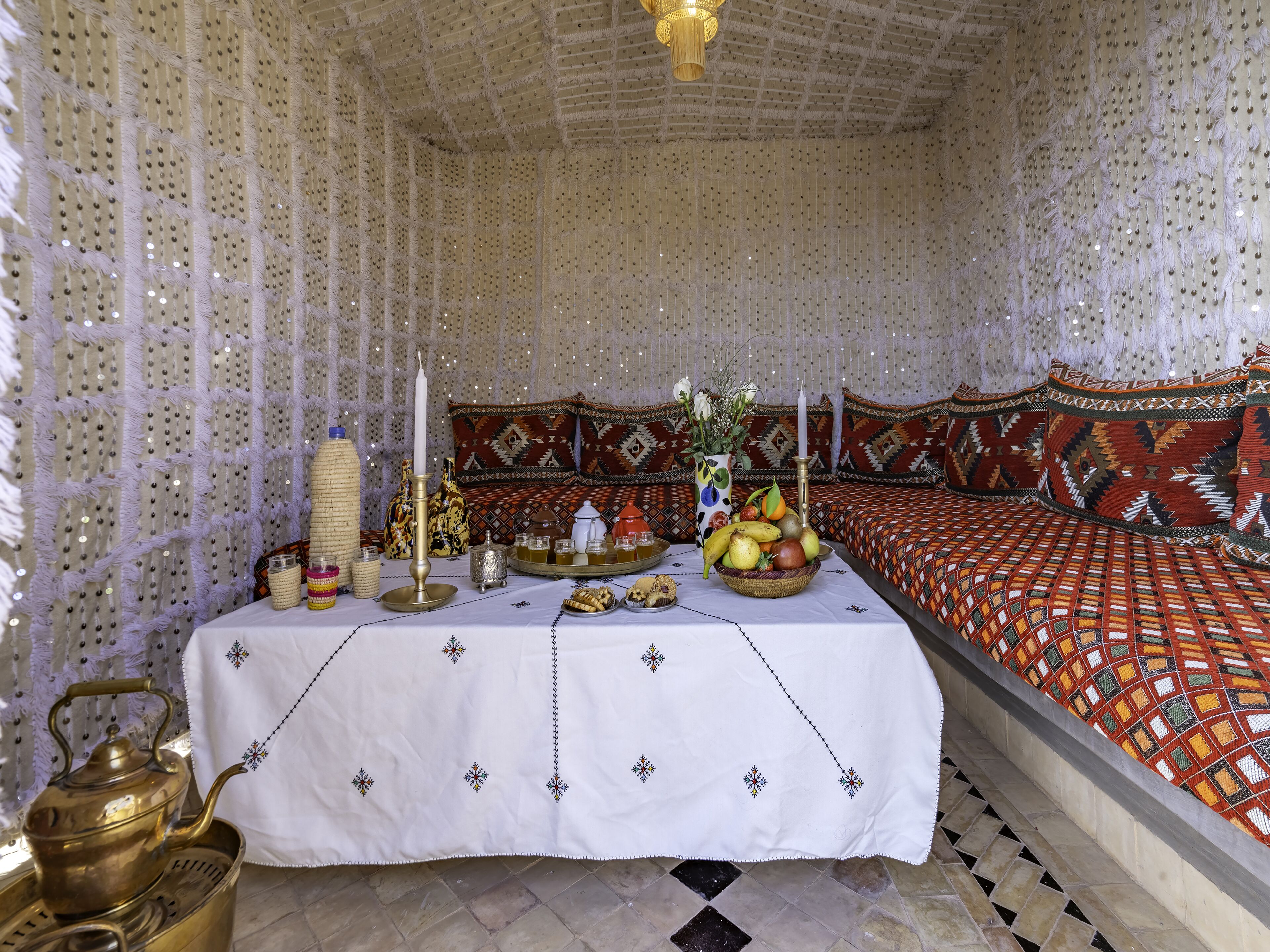 A room with a patterned bed, a table with a white cloth and decorative items, and a patterned wall.