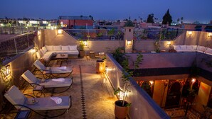 A rooftop terrace with lounge chairs, potted plants, and ambient lighting. - Riad Touda (Marrakech)
