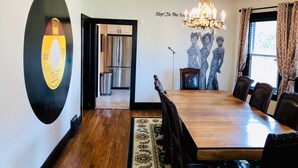A dining room with a wooden table, chairs, a chandelier, a wall-mounted record player, and a kitchen in the background. - Motown BNB . Experience Detroit in style. (Detroit)