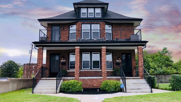 A two-story brick house with a balcony, numbered 2704 and 2702, featuring a front porch and a small front yard. - Motown BNB . Experience Detroit in style. (Detroit)