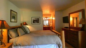 Un dormitorio con cama, mesitas de noche, cómoda, espejo y un pasillo que da a un baño.