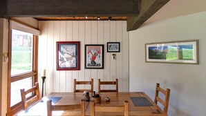 Un comedor con mesa y sillas de madera, cuadros en la pared y una ventana con vistas a la vegetación.