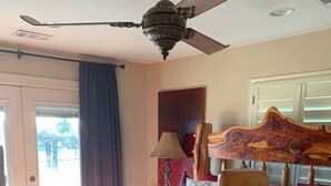 Une chambre à coucher avec une tête de lit en bois, un grand lit recouvert d’une couverture rouge, un ventilateur de plafond et une vue sur l’extérieur par une porte.