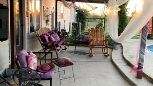 Un patio couvert avec un espace salon extérieur, comprenant une chaise en métal et une chaise en bois avec des coussins.