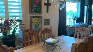 Un coin repas avec une table en bois, six chaises, un lustre et une croix accrochée au mur.