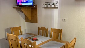 Un coin repas avec une table et des chaises en bois, un téléviseur fixé à une étagère et une petite plante en pot accrochée au mur.