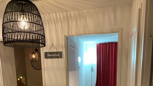 Une pièce comprenant un lit, un luminaire suspendu et une porte donnant sur une autre pièce.