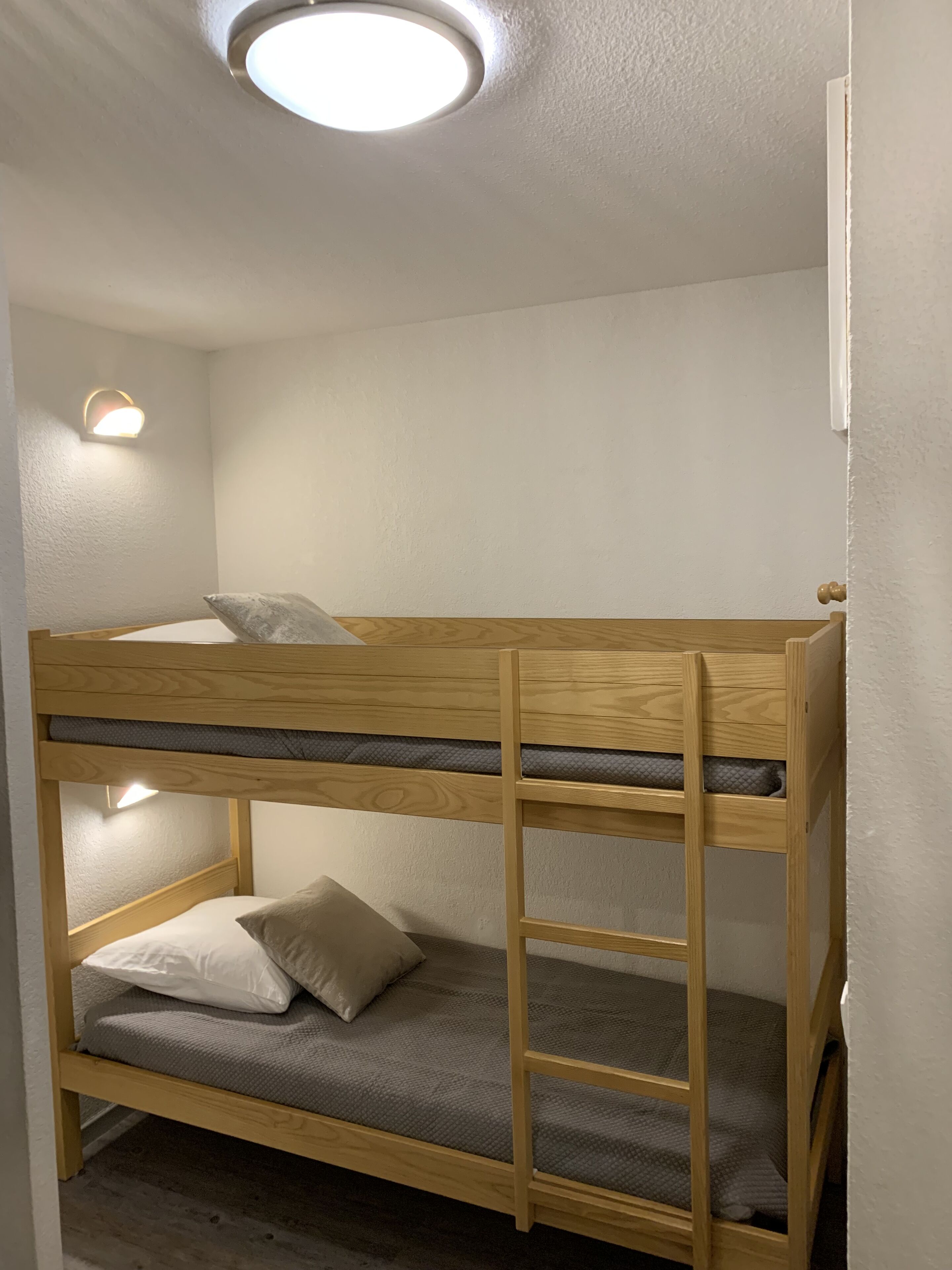 A bunk bed with a ladder, a wall-mounted light, and a ceiling light.