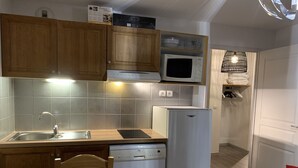 Une cuisine de taille réduite, dotée de meubles en bois, d’un four à micro-ondes, d’un réfrigérateur et d’un lave-vaisselle.