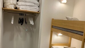 Un lit superposé avec une étagère au-dessus, où sont pliées des couvertures et des serviettes.