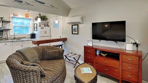 A living room with a sofa, a small table, a television, and a kitchen area in the background.