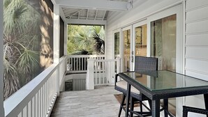 A covered porch with a glass table and chairs, white railings, and a ceiling fan.