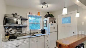 A modern kitchen with white cabinets, a built-in microwave, a refrigerator, and a wooden island with bar stools.