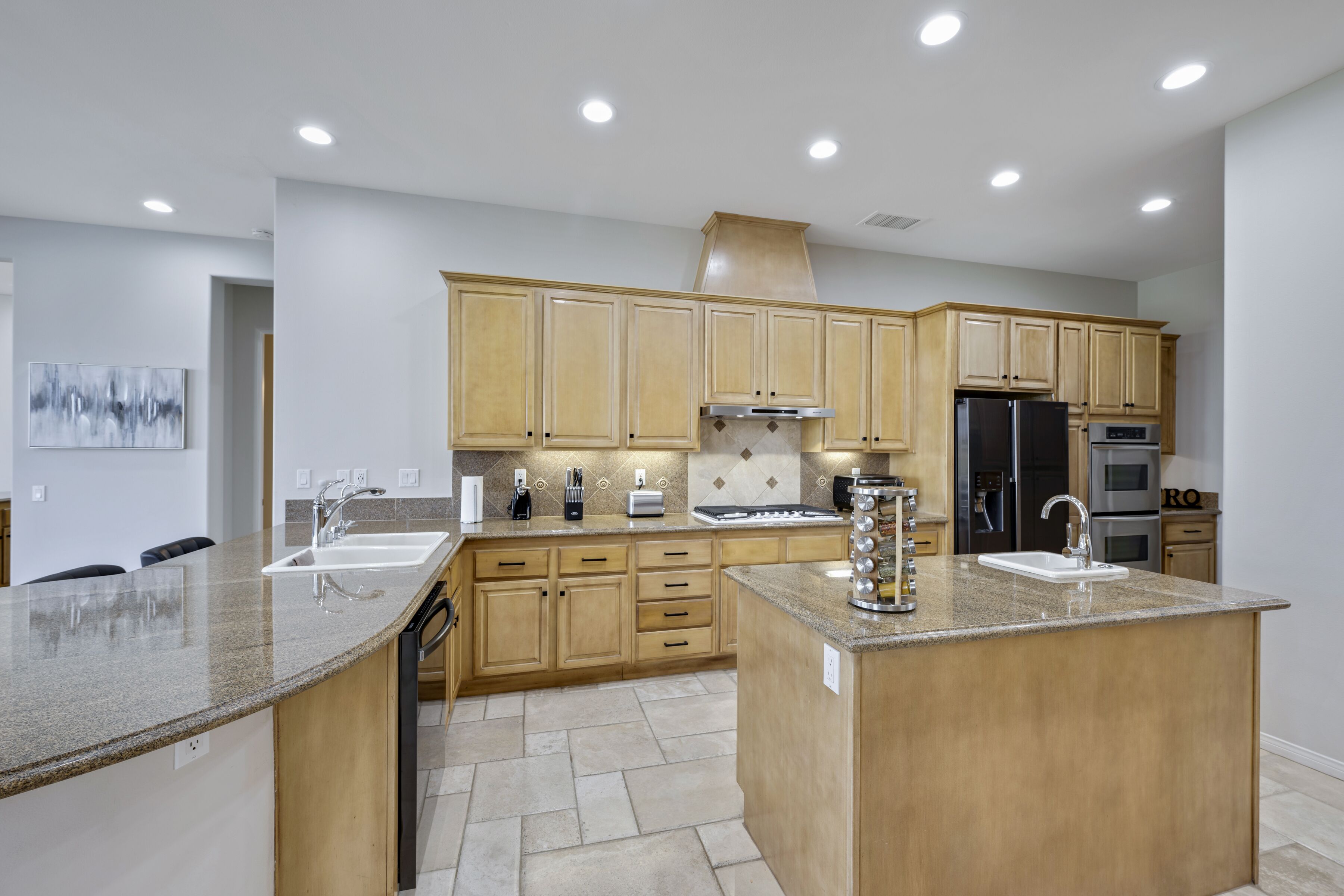 Una cocina moderna con encimeras de granito, armarios de madera y electrodomésticos de acero inoxidable, además de luces empotradas en el techo.