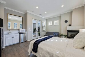A bedroom with a bed, a dresser, a microwave, a fireplace, and a large mirror.