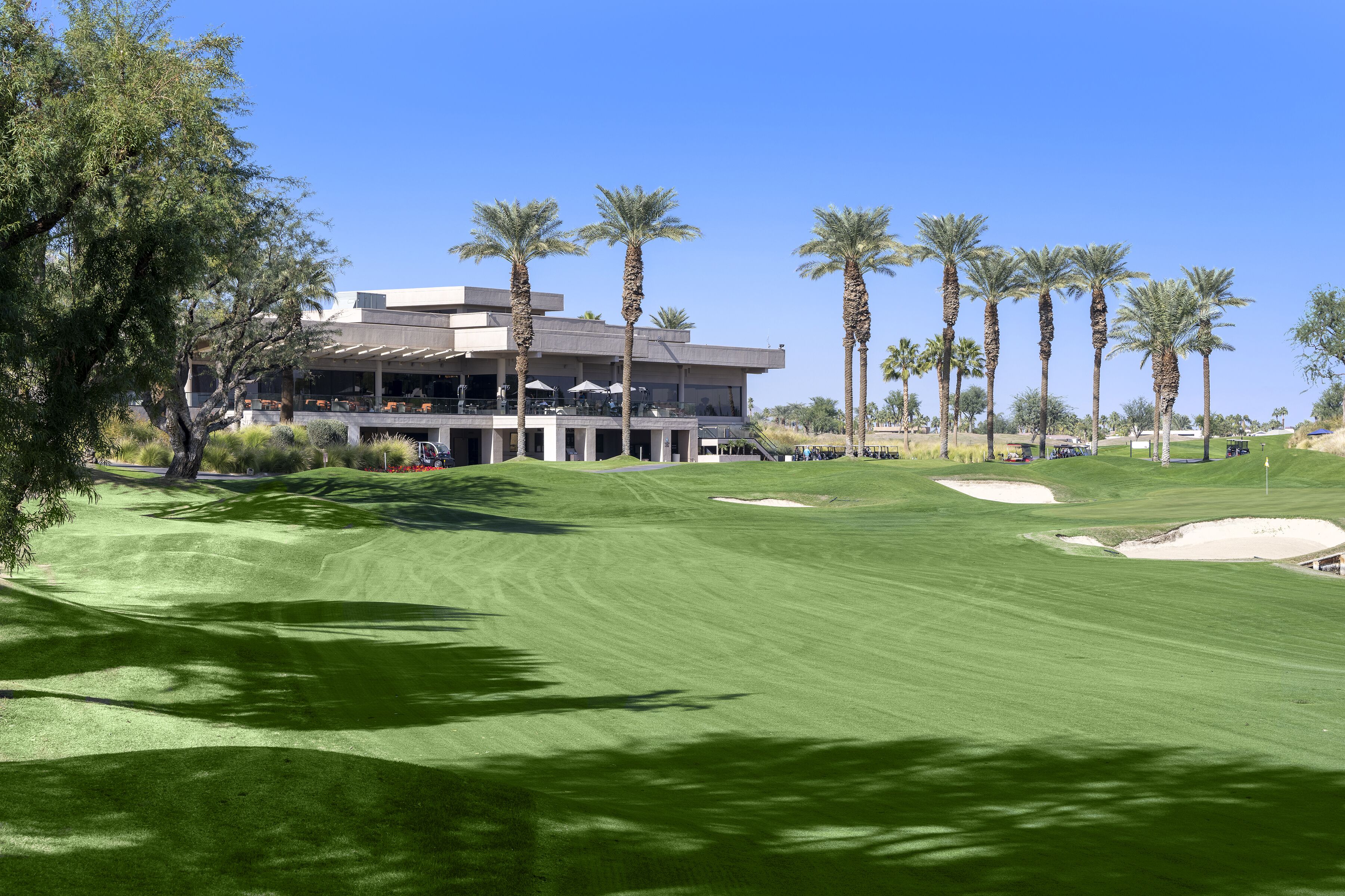 A golf course with a building in the background, palm trees, and a clear sky.