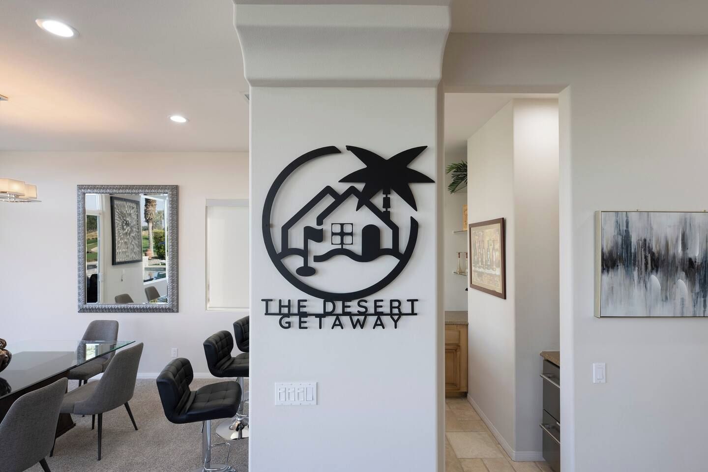 Ein modernes Interieur mit einem Schild, das 'The Desert Getaway' zeigt, und einem Essbereich mit Stühlen und einem Glastisch.