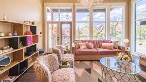 Un salon chaleureux avec un canapé rose, des fauteuils moelleux, une table basse en verre et une bibliothèque.